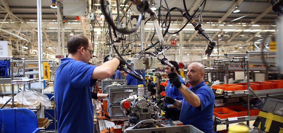 several workers in a factory controlling robotic arms
