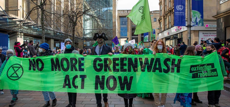 Protesters holding a green sign stating "no more greenwash act now."