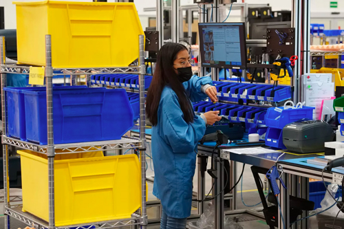 woman in a mask in a factory sorting through small bins